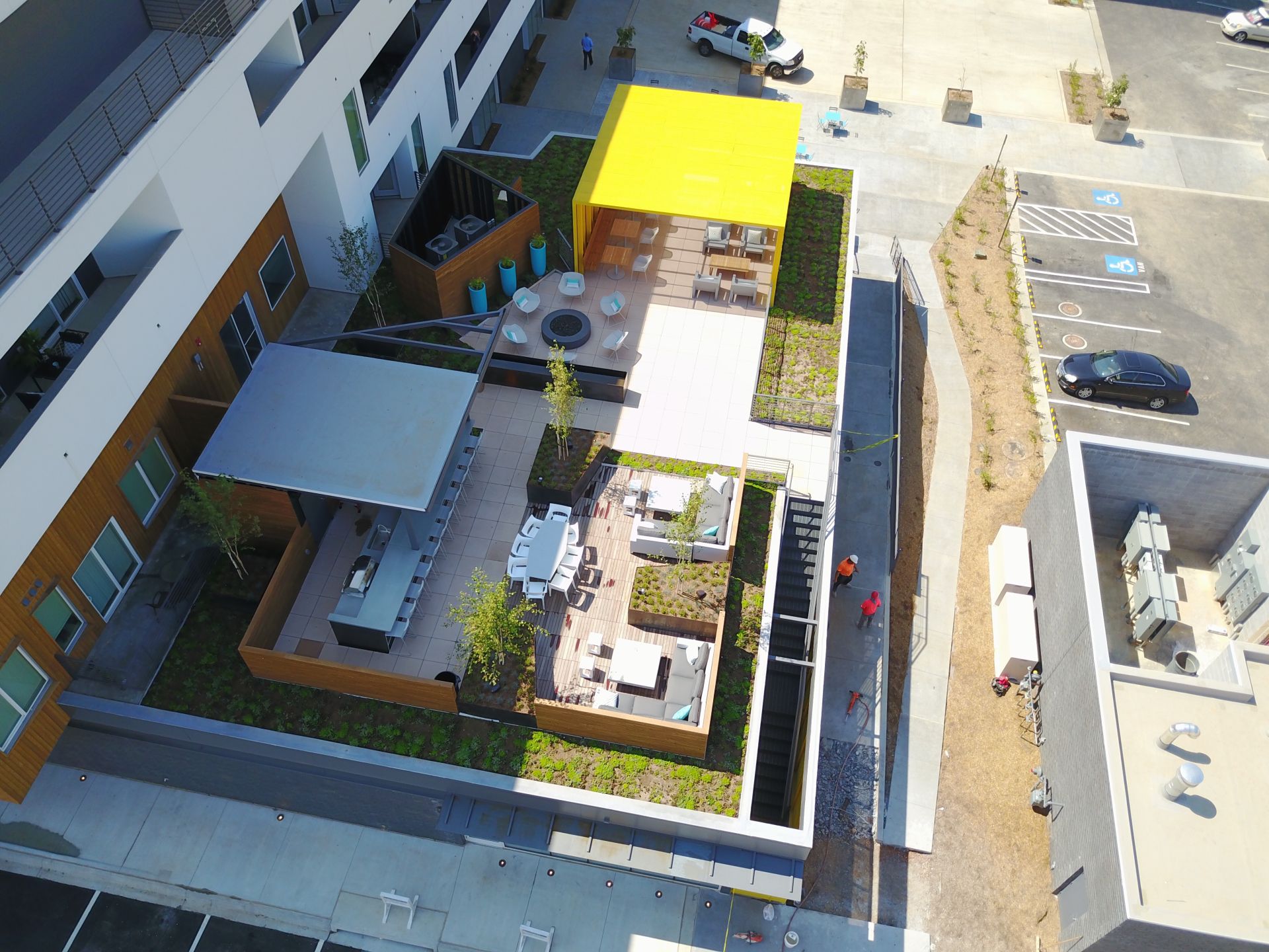 Aerial view of an outdoor building courtyard with lounge seating, a shaded bar, a yellow pavilion, and landscaping.