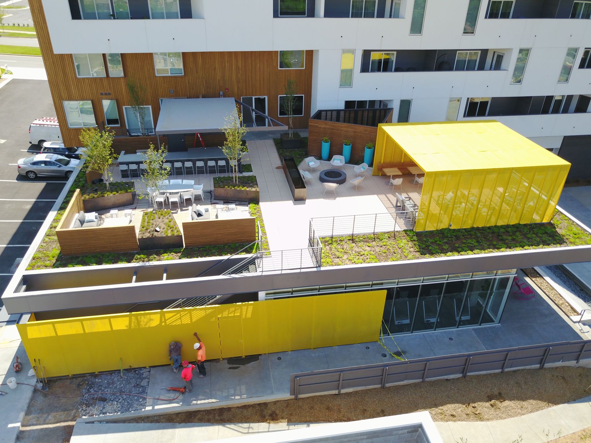 Aerial view of a multi-level building with a yellow metal canopy, rooftop patio, and modern outdoor seating area.