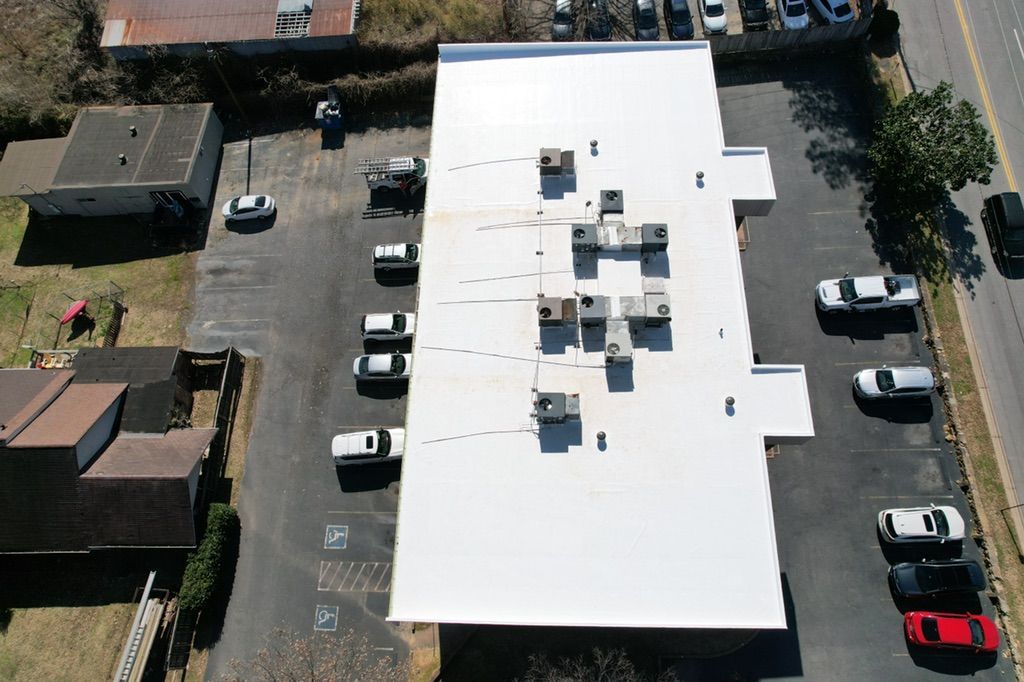 An aerial view of a building with a white roof, surrounded by a parking lot with several vehicles parked on both sides.