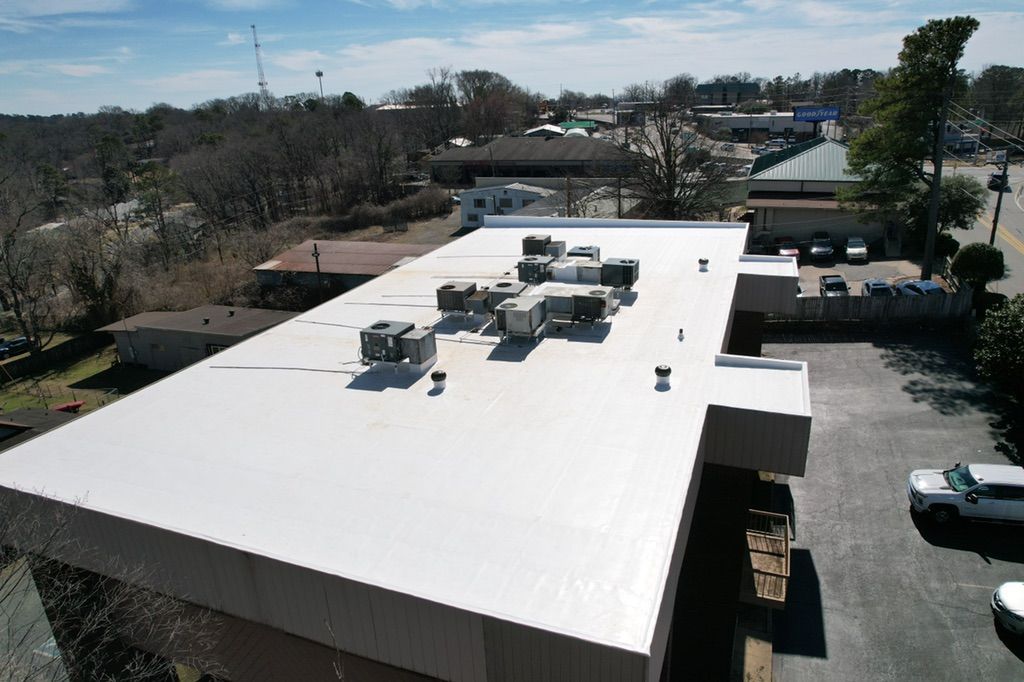 An aerial view of a white, flat commercial roof featuring multiple HVAC units, surrounded by a parking lot and buildings.