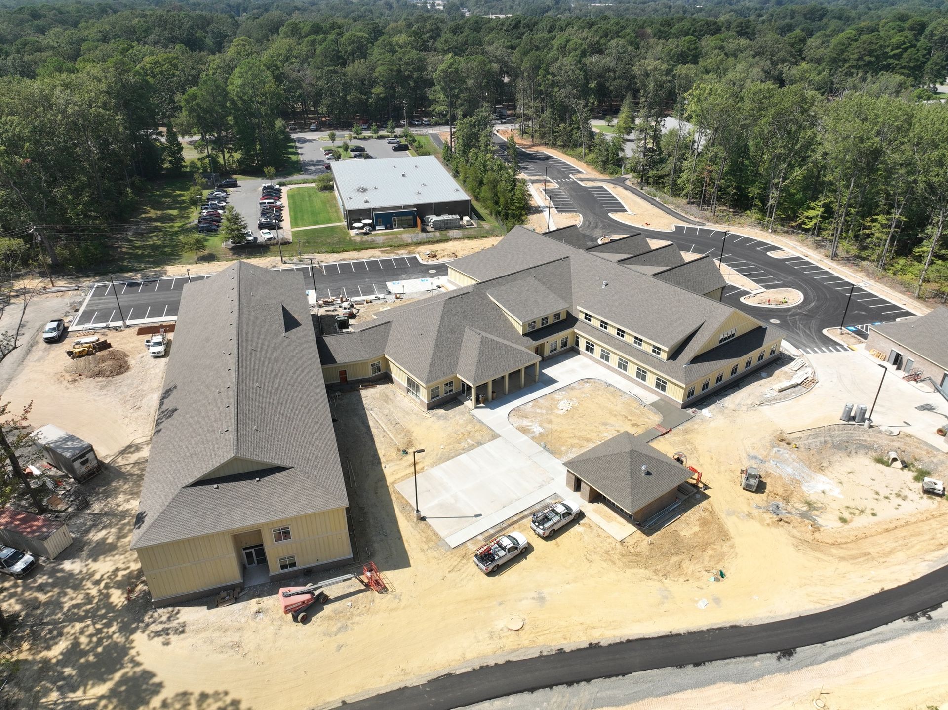 An aerial view of a construction site featuring multiple beige buildings with grey shingled roofs and surrounding roads.
