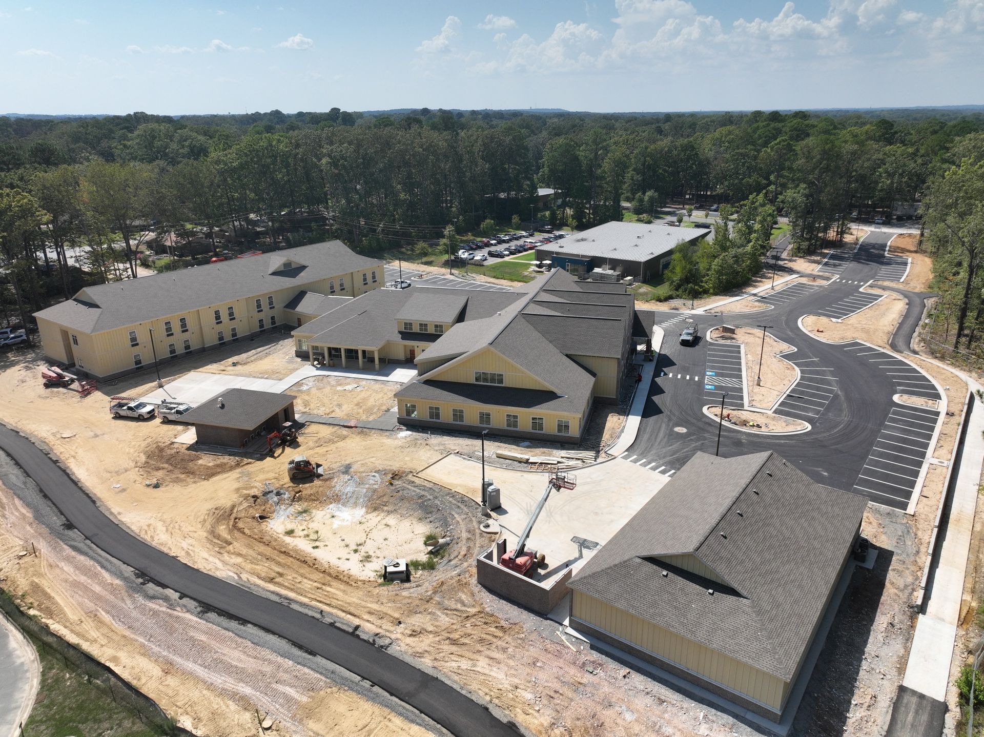 Aerial view of a complex of beige buildings under construction, surrounded by paved roads and dirt landscaping.