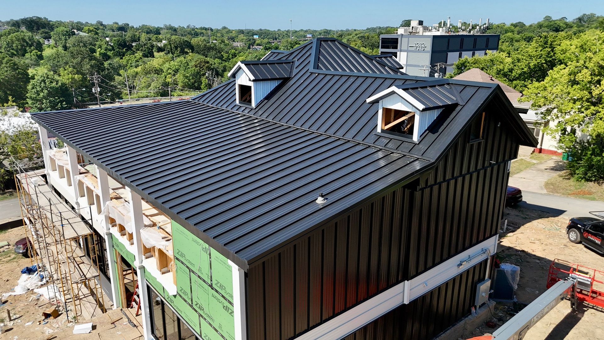High-angle view of a building under construction, featuring a newly installed black metal roof and matching wall panels.