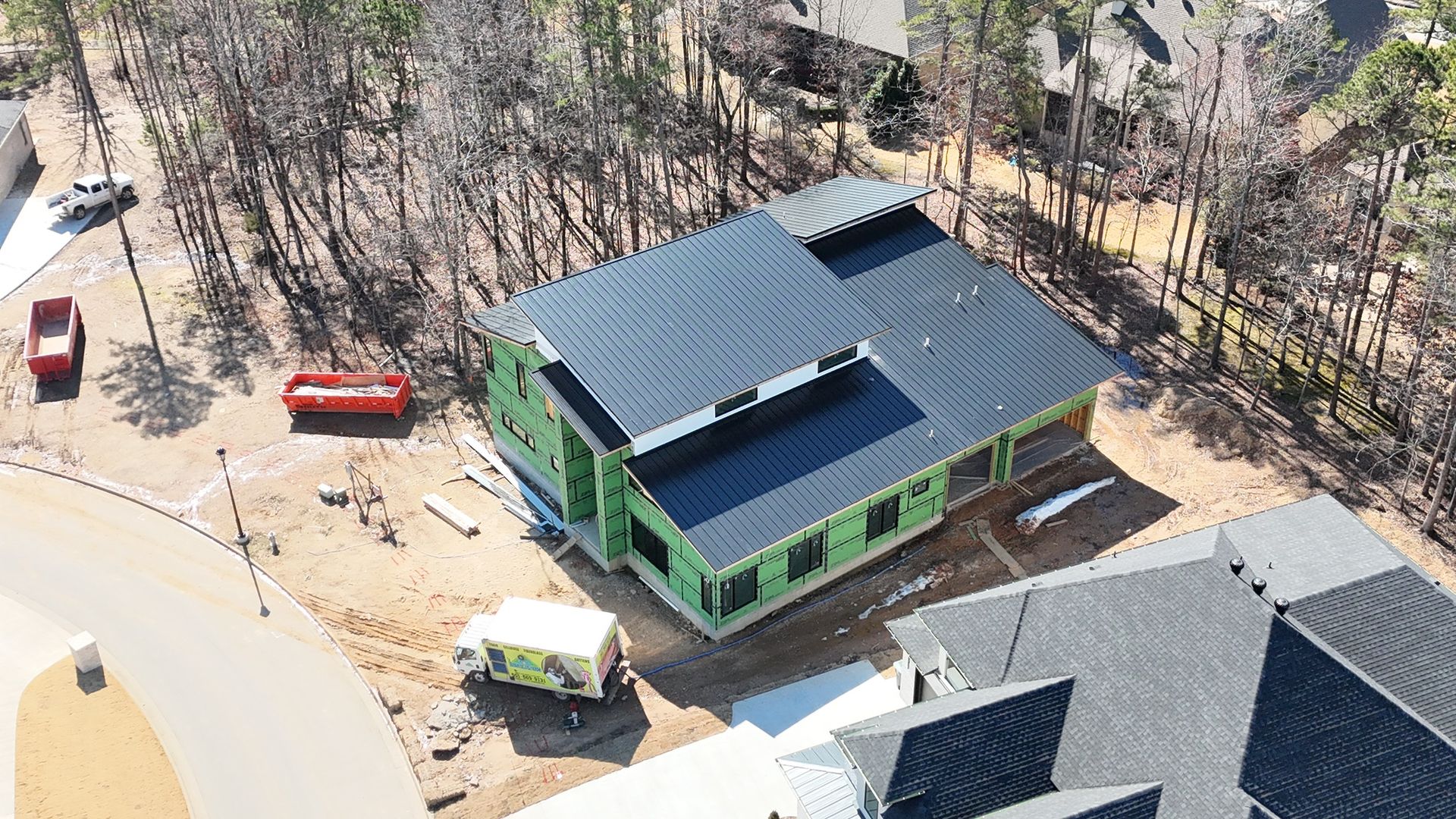 An aerial view of a new residential home under construction, featuring green exterior sheathing and a black metal roof.