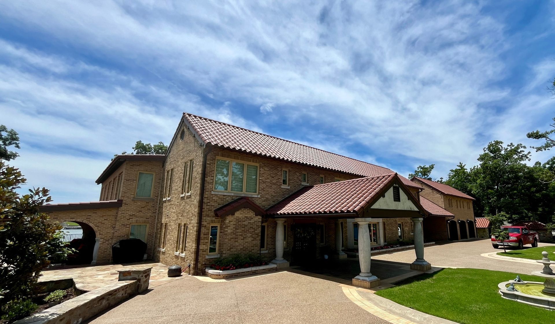 A two-story stone mansion with a tile roof and covered entrance portico, surrounded by trees and a gravel driveway.