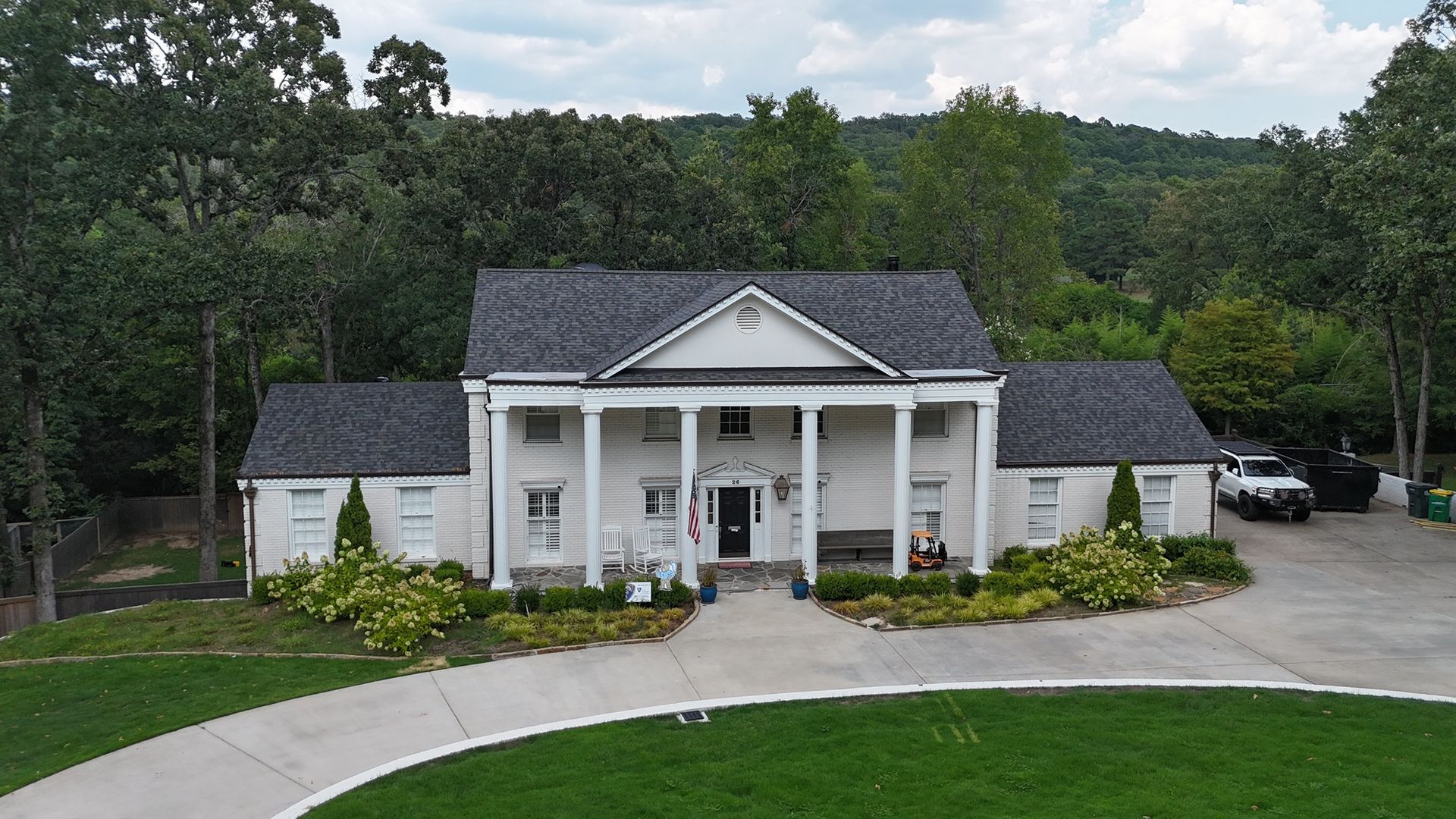 A white two-story house with a columned portico and a curved driveway in a wooded setting.