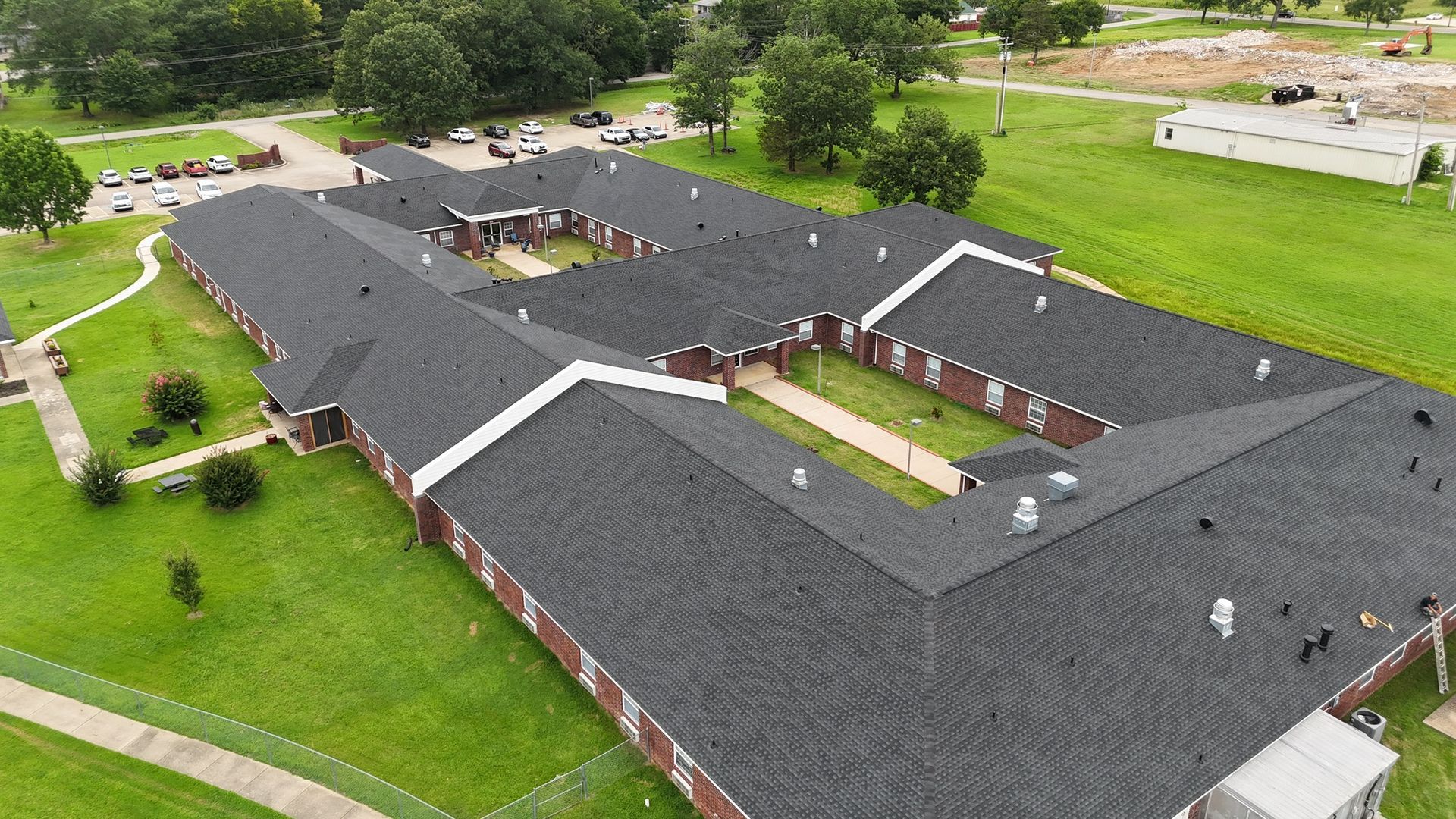 An aerial view of a single-story brick building with a dark shingled roof, surrounded by green lawns and walkways.