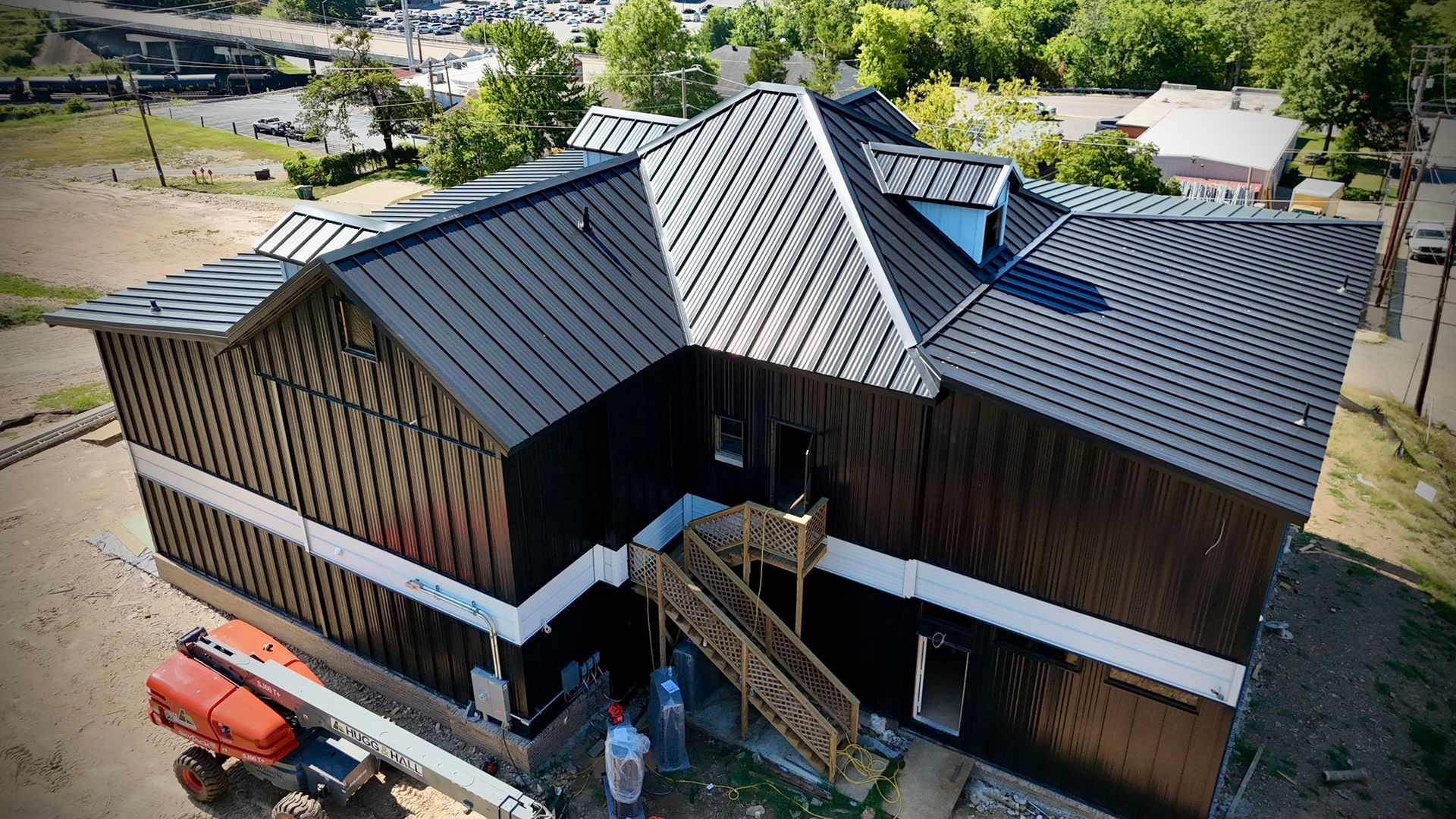 An aerial view of a building under construction, featuring a dark-colored metal roof and exterior walls wrapped in black.
