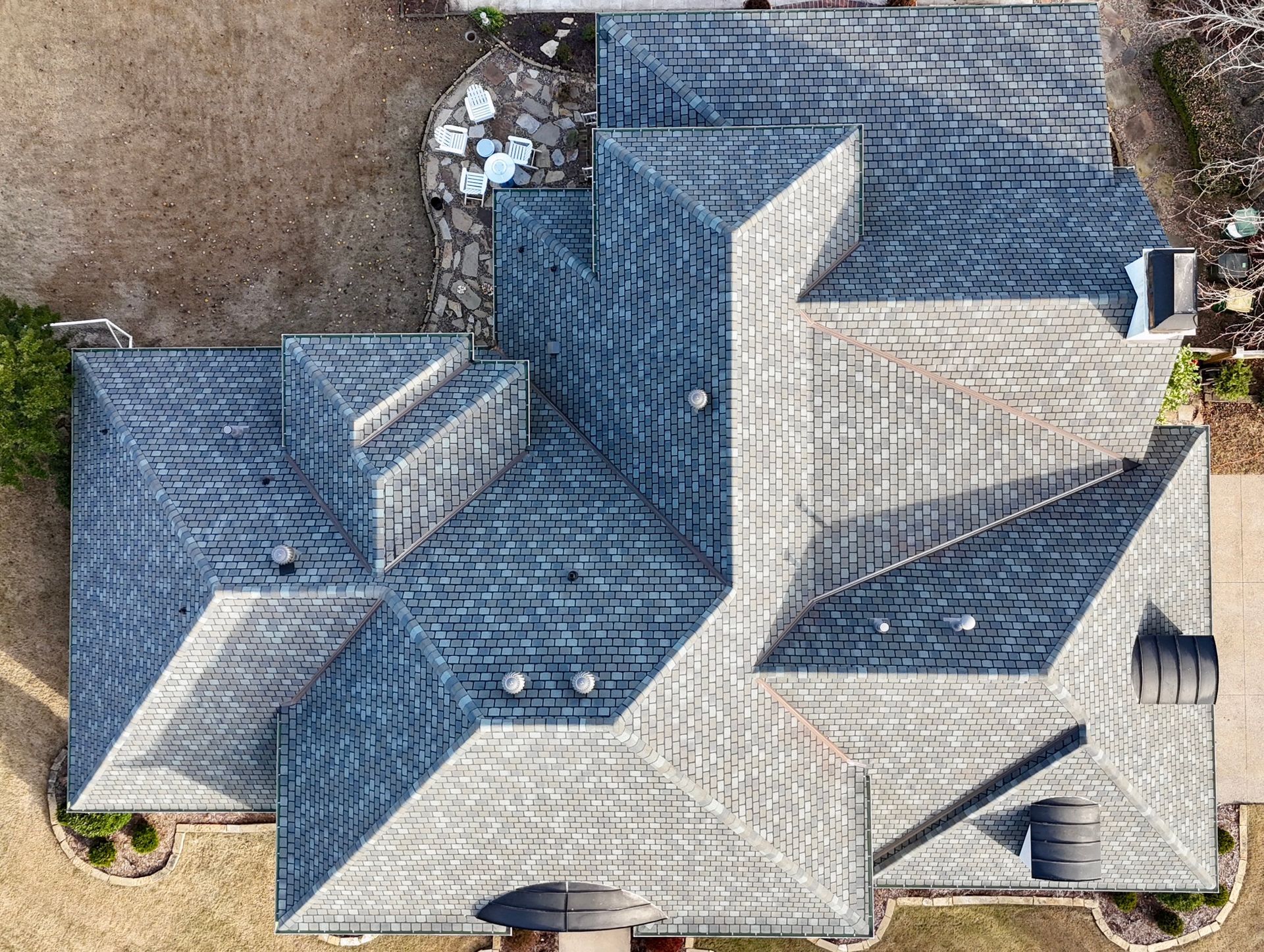 An aerial view of a multi-gabled, shingled residential roof with several vents and chimneys.