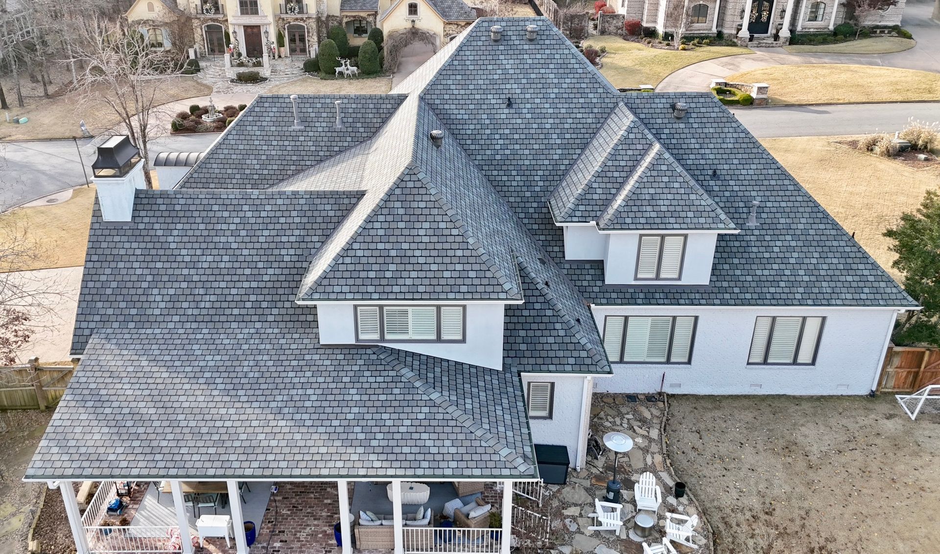 Aerial view of a house with a dark grey roof and a covered patio, set in a residential neighborhood.