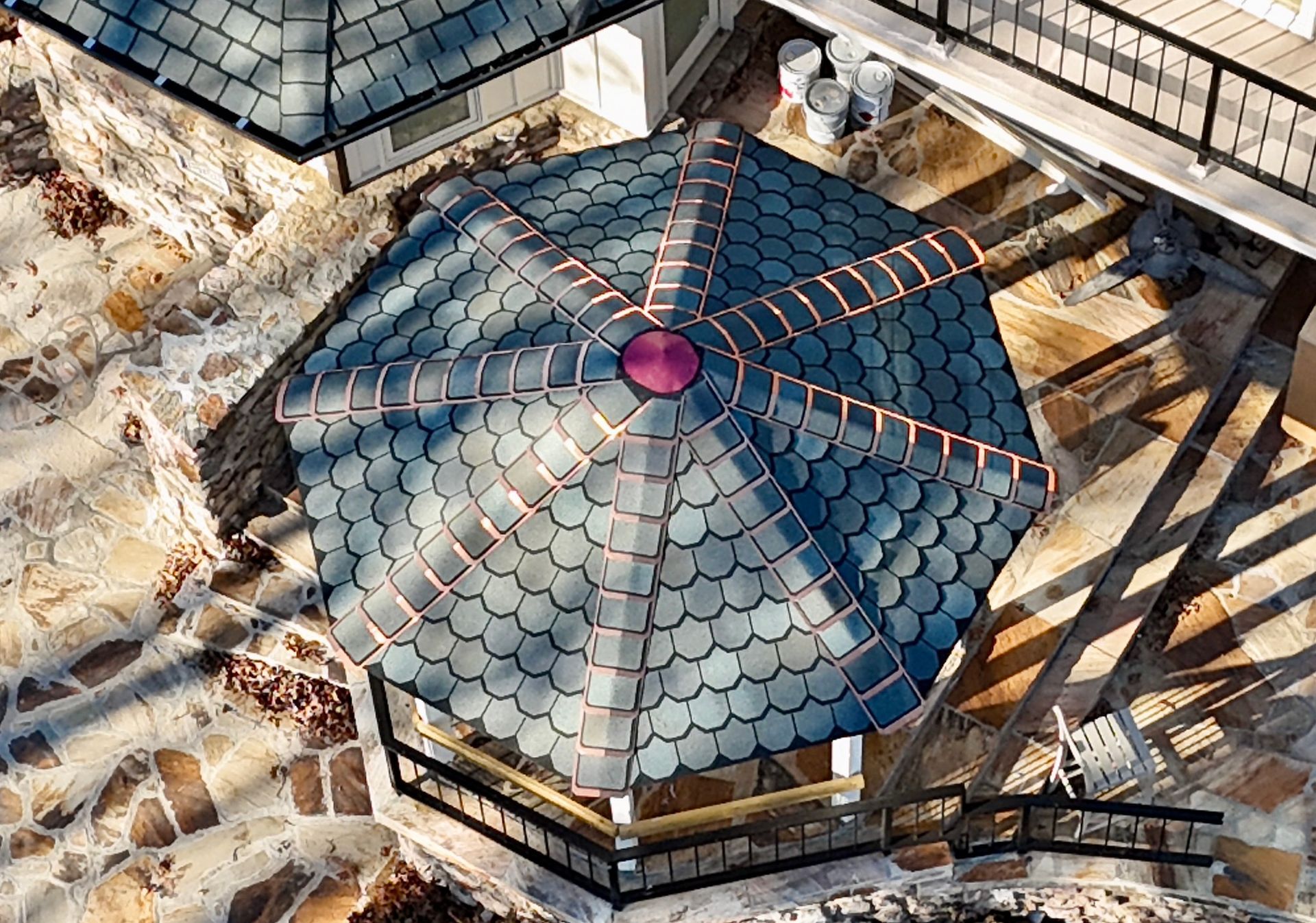 An elevated view of a gray, scalloped-shingle octagonal gazebo roof with copper flashing, set on a stone patio.