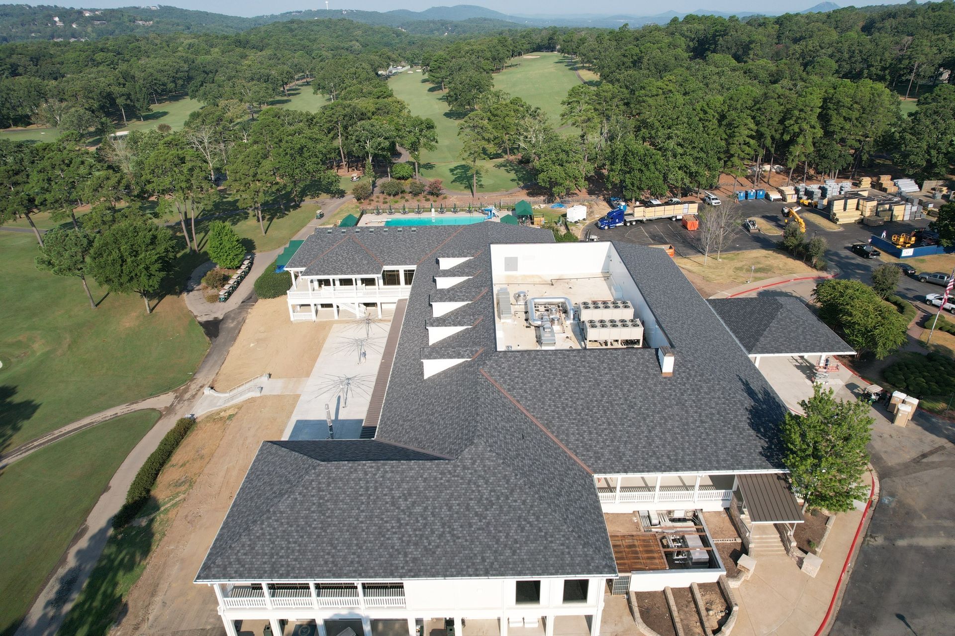 Aerial view of a white multi-level building with a dark shingled roof, located next to a green golf course and trees.