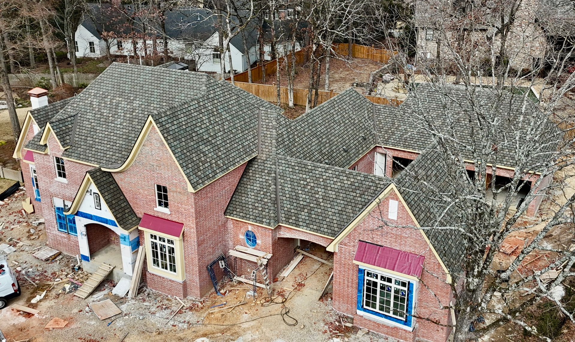 An aerial view of a large residential house under construction, featuring red brick walls and a shingled roof.