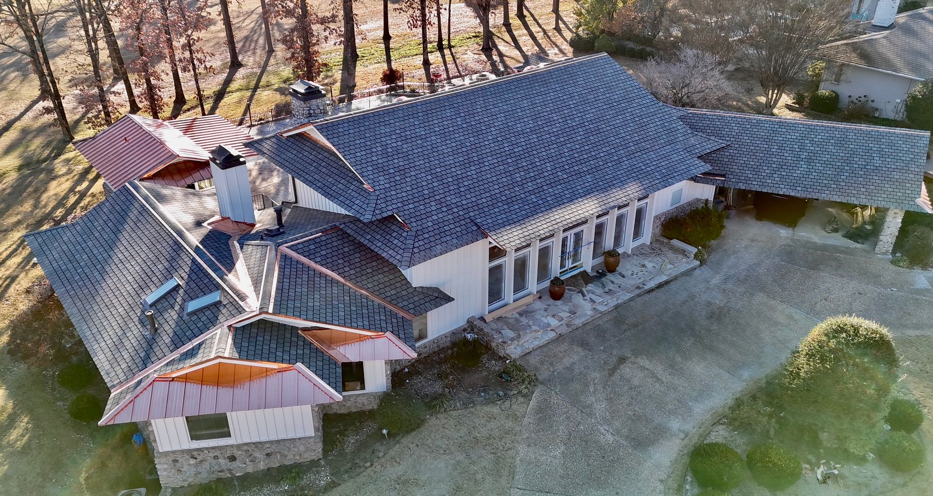 An aerial view of a suburban house with a dark shingled roof, stone accents, and a large gravel driveway.